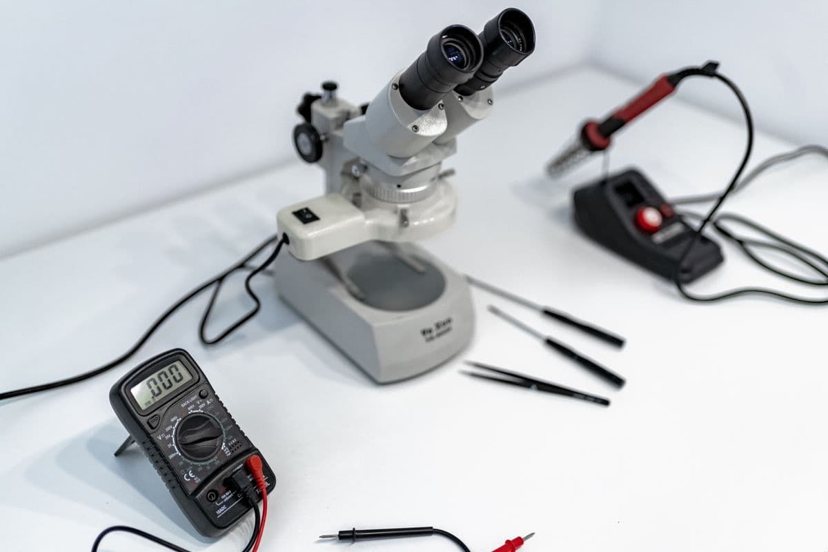 Technician tracing circuit paths on a board under a workbench microscope