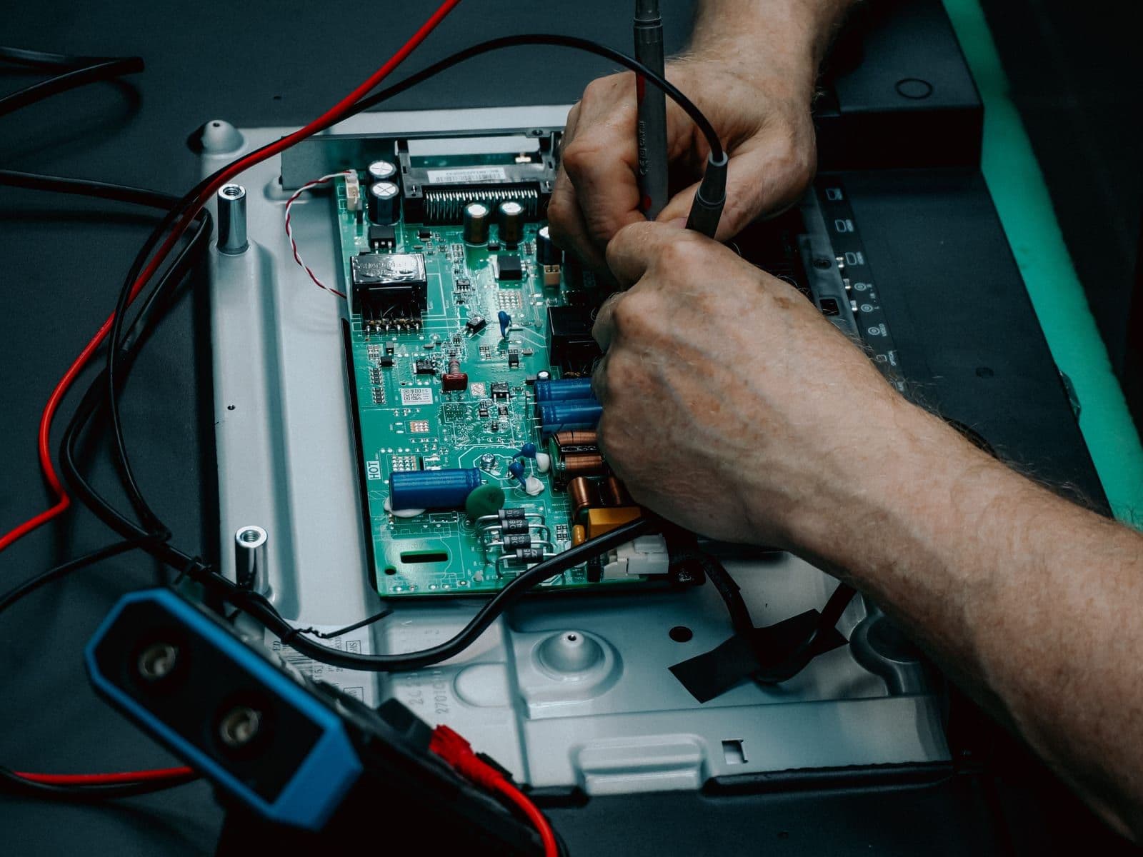 Component-level work on a populated circuit board with a multimeter probe